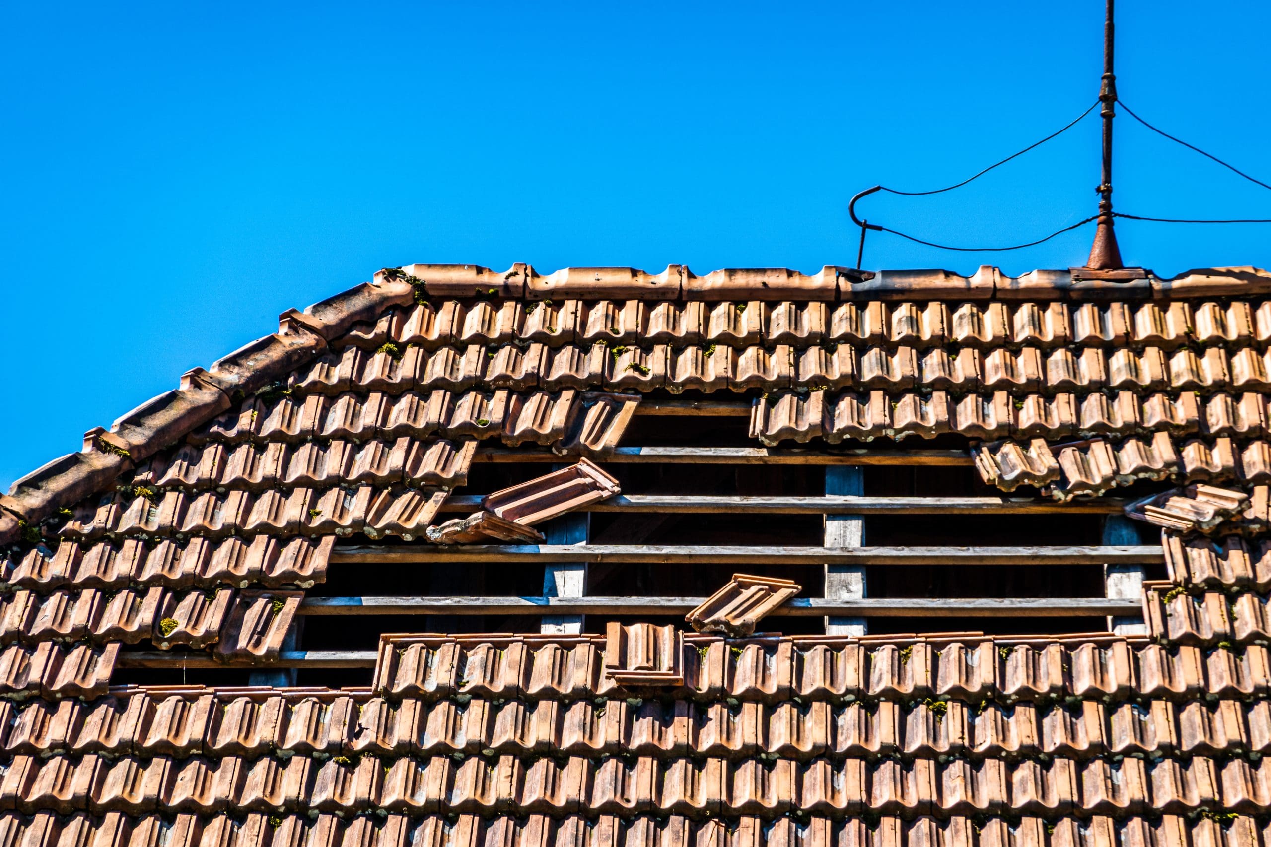 A roof with damaged tiles arranged in the shape of a smiling face against a clear blue sky. Antennas can be seen on top of the roof.