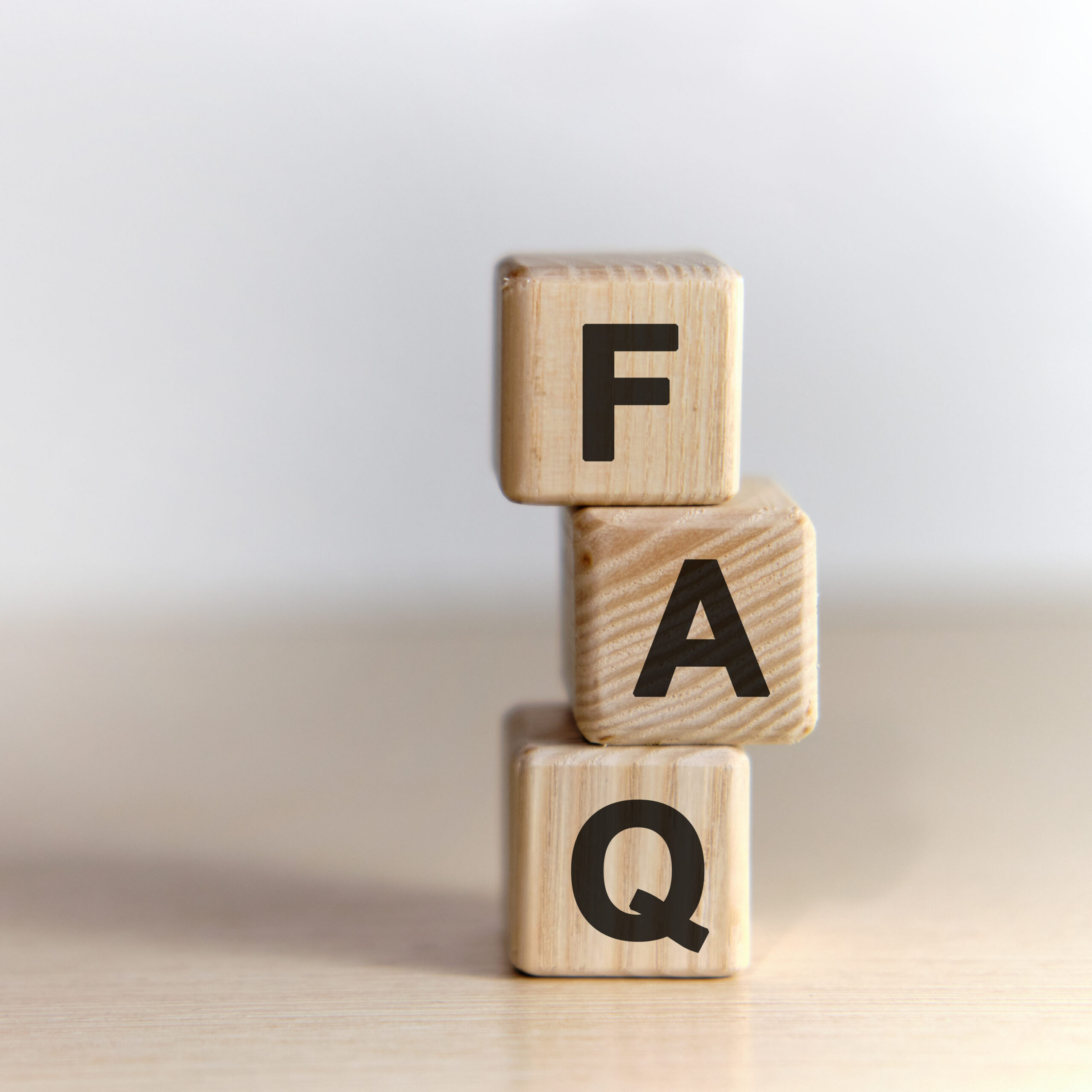 Three wooden blocks stacked vertically on a light surface, each displaying a large black letter; from top to bottom, the blocks spell out "FAQ" against a plain background.